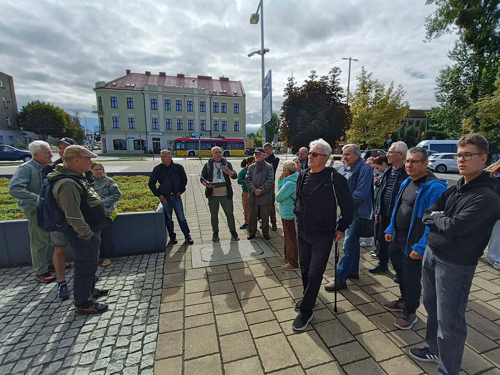 Spacer historyczny po dworcu w Oświęcimiu – początek trasy - NaszOświęcim - informacje i wydarzenia. Przewodnik z notatkami opowiada grupie uczestników spaceru historycznego na placu przy dworcu w Oświęcimiu