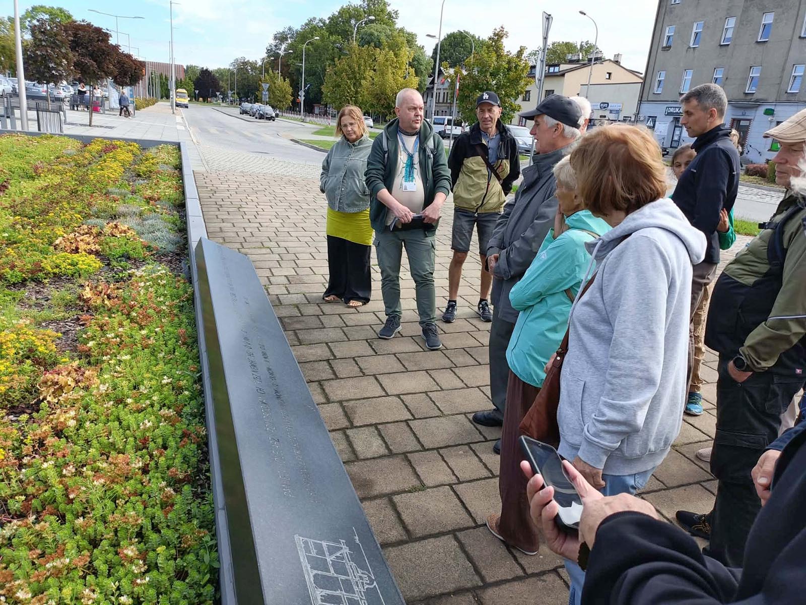 Tablica pamiątkowa przy dworcu w Oświęcimiu - NaszOświęcim - informacje i wydarzenia. Uczestnicy spaceru historycznego przy kamiennej tablicy z inskrypcją i rysunkiem technicznym w Oświęcimiu